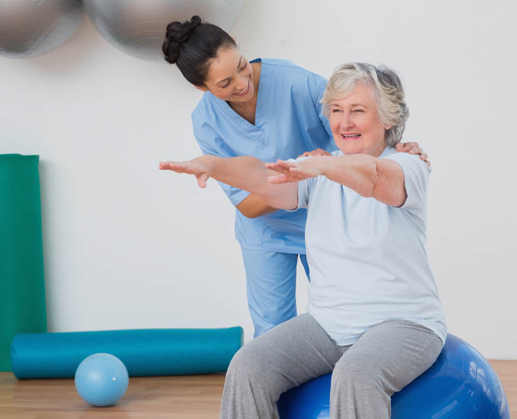 A senior woman sits on a balance ball and works with a physical therapist