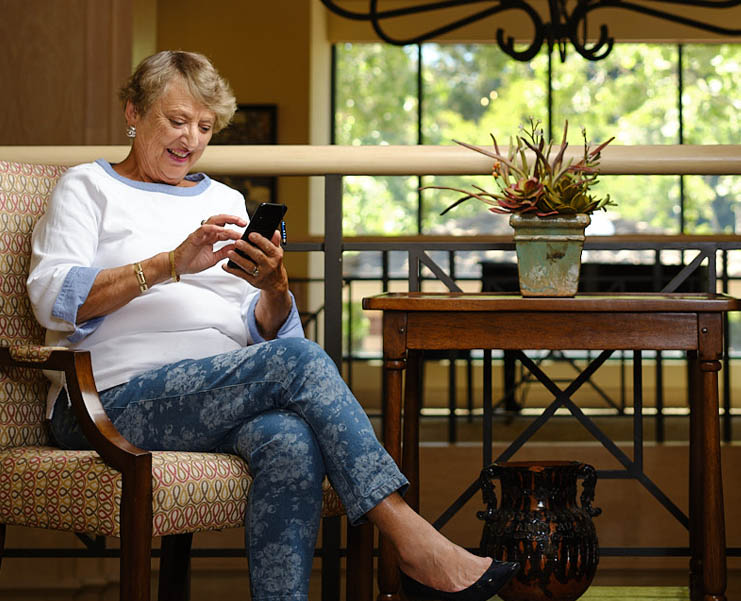 A senior woman sits in an armchair and looks at a smart phone